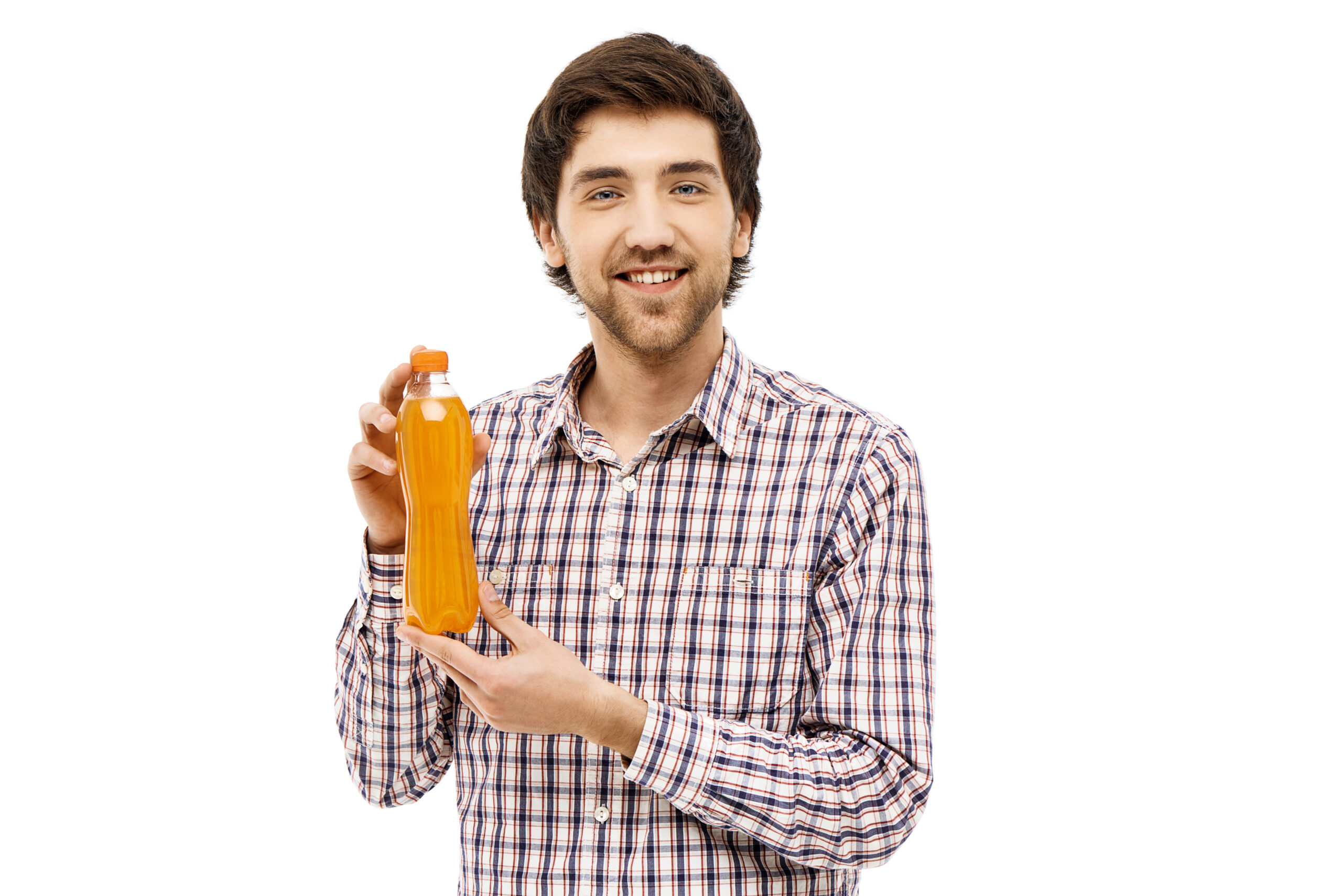 Young handsome cheerful man in plaid shirt showing plastic bottle with orange beverage. Looking at camera. Isolated on white background.